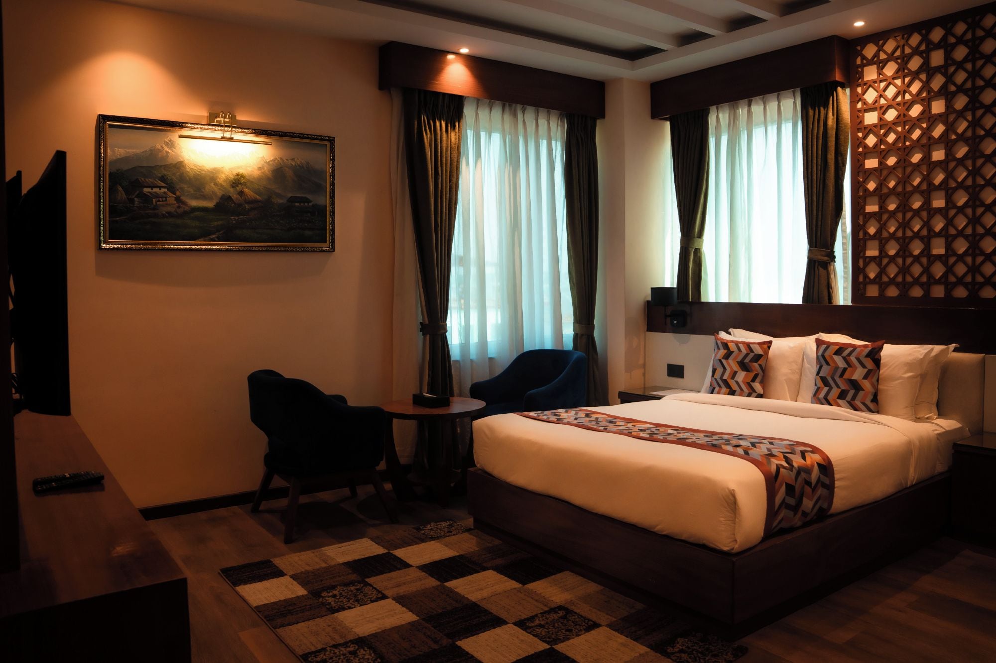 A hotel room with a bed, a desk, a chair, and a painting on the wall.