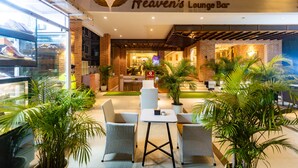 Et loungeområde med fletningsmøbler, plantede planter og et skilt, der siger "Heaven's Lounge Bar".