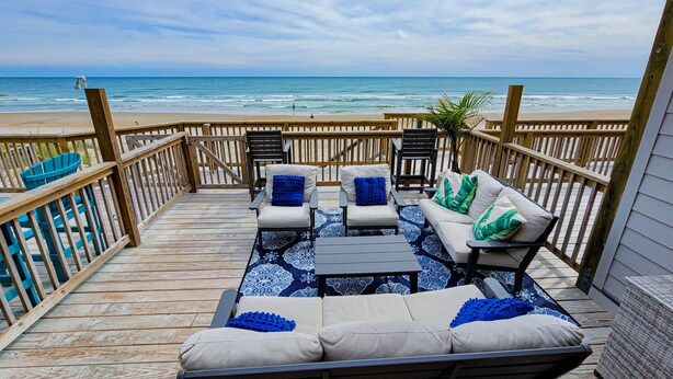 Eine Holzterrasse mit Gartenmöbeln mit Blick auf einen Strand.