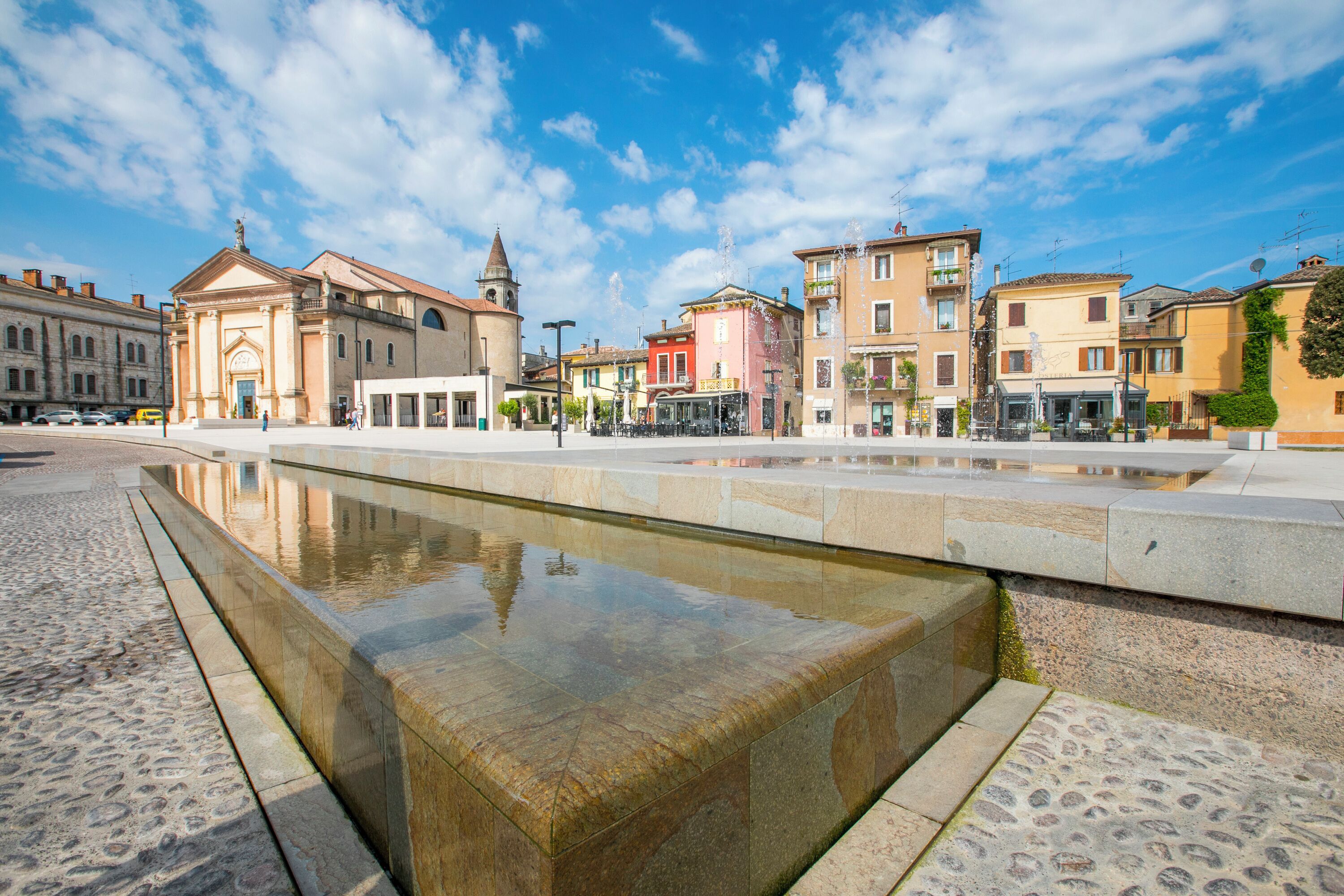 Una plaza con fuente reflectante, edificios históricos y cielo despejado.