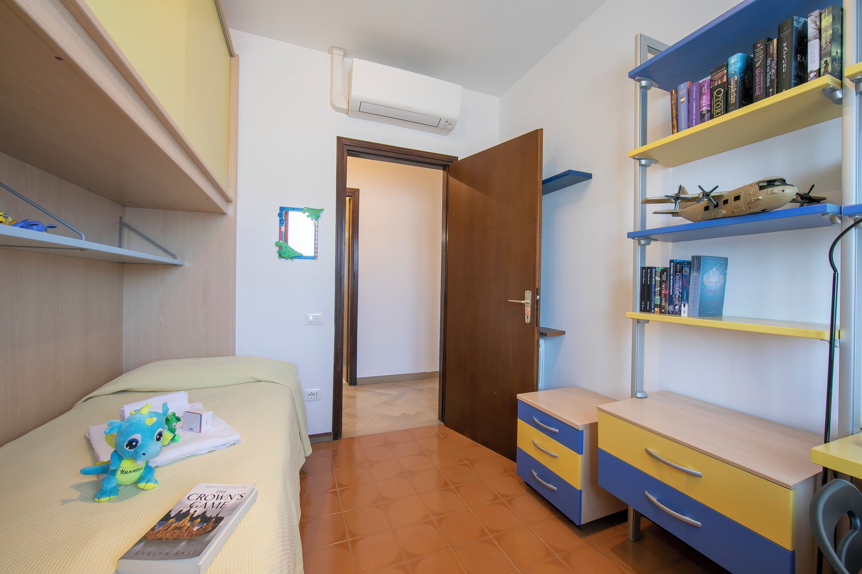 A room with a bed, a desk, a bookshelf, and a door leading to another room.