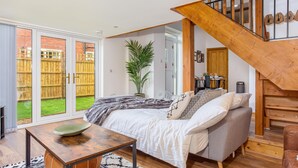 Een ruime woonkamer met een groot bed, een houten trap en uitzicht op een omheinde tuin.