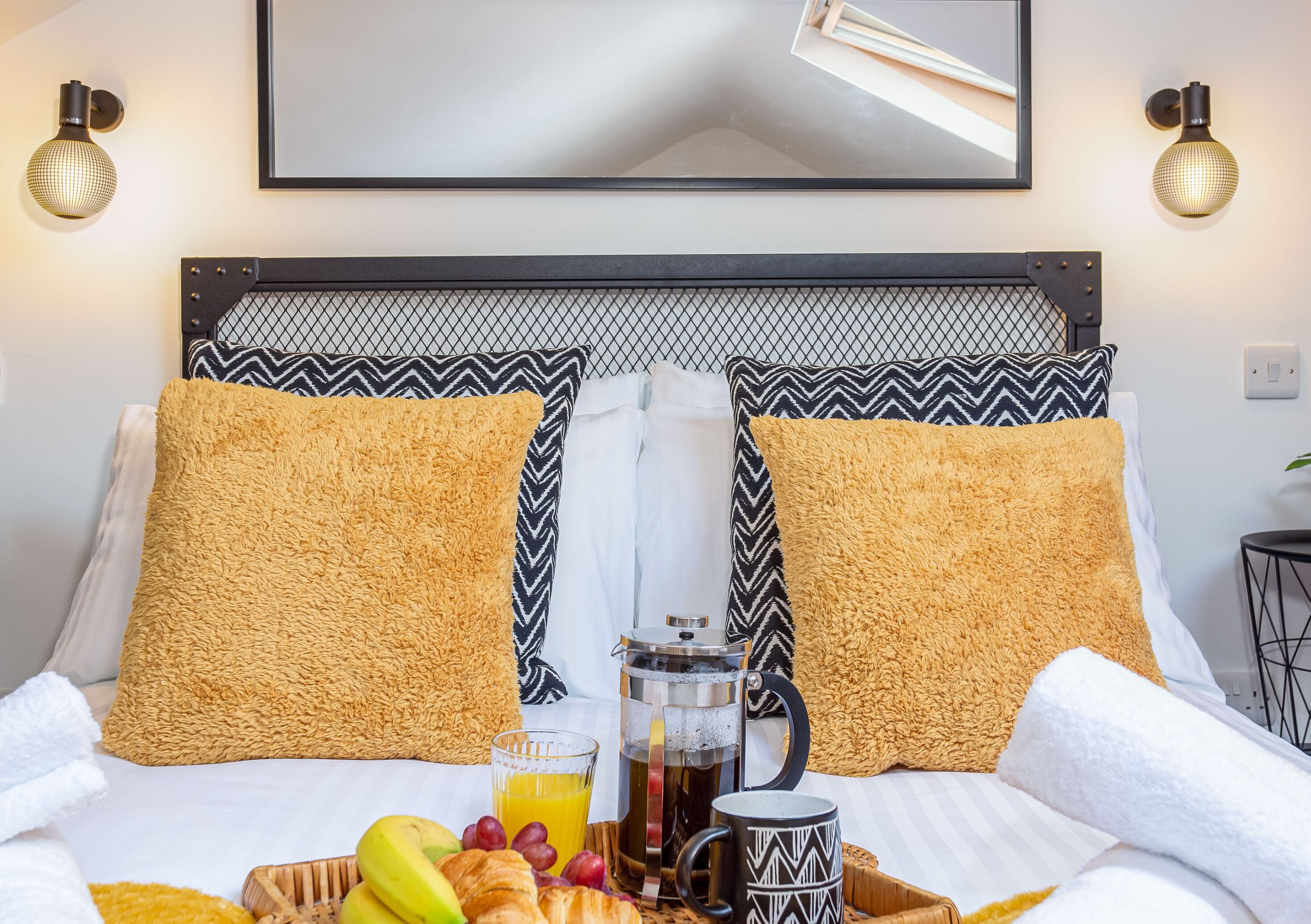 A neatly made bed with a patterned headboard, a tray with breakfast items, and a framed picture above.