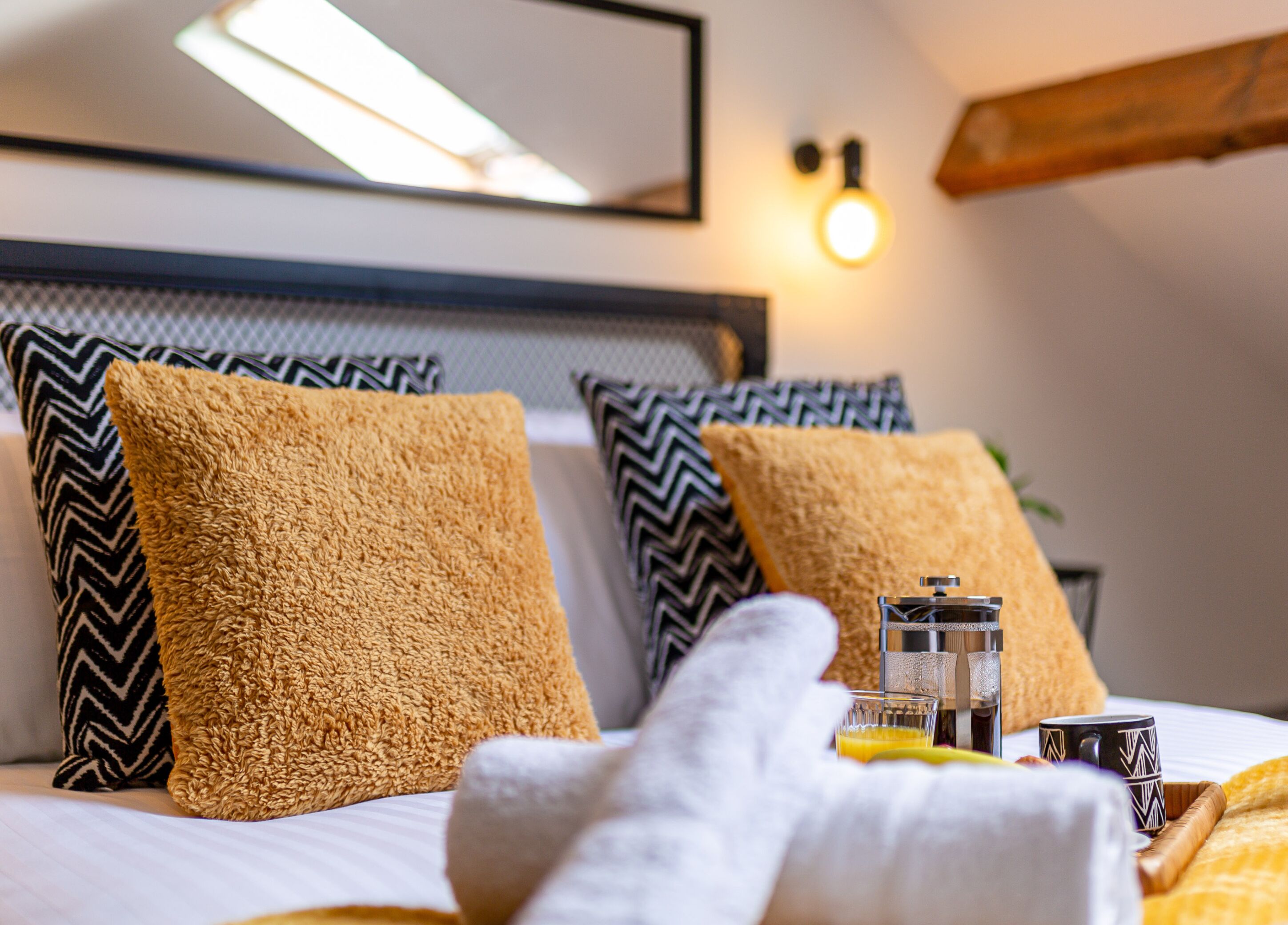 A neatly made bed with two pillows, a glass of orange juice, a bottle, and a mug on the bedside table.