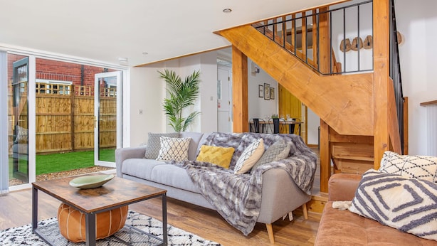 Een moderne woonkamer met een grijze bank, een houten salontafel en een trap met een houten leuning.
