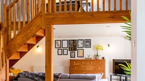 Een houten trap die leidt naar een woonkamer met een bank, een televisie en een muur met ingekaderde foto’s.