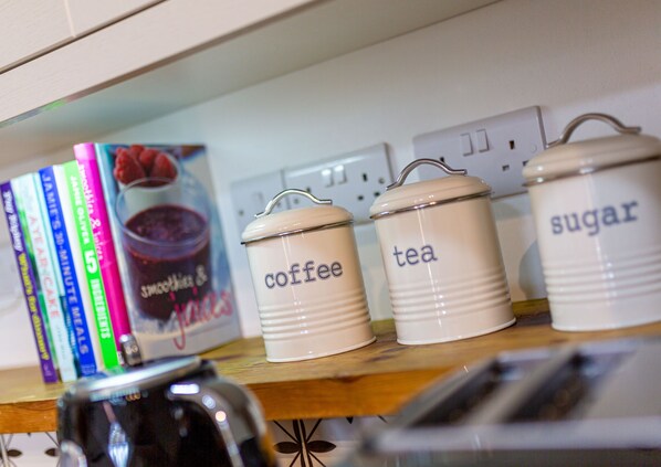 Estanterías de cocina con recipientes etiquetados para café, té y azúcar, y un libro de cocina titulado