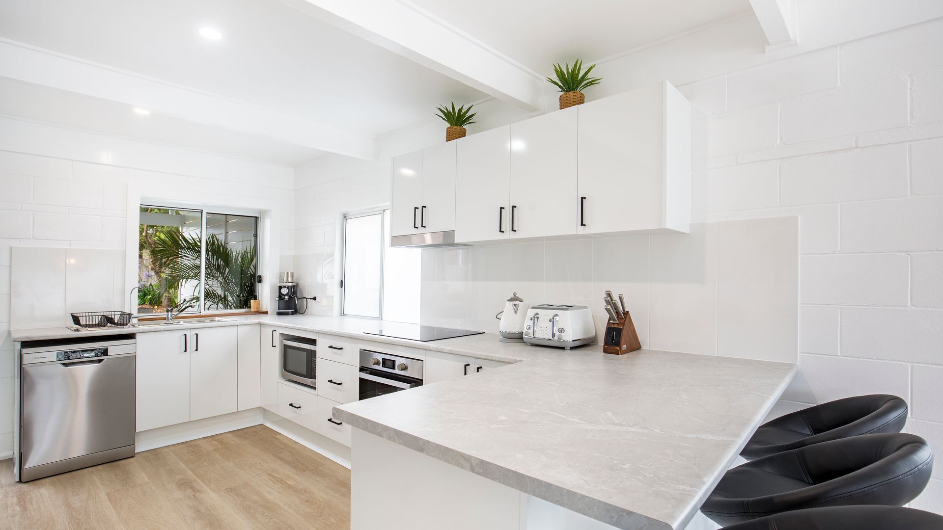 A modern kitchen with white cabinetry, a built-in oven, a coffee machine, and a toaster.