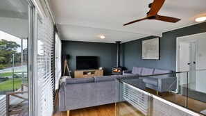 Un salon moderne avec un canapé, un téléviseur, une cheminée et un balcon doté d’une balustrade en verre.
