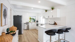 Une cuisine moderne avec des meubles blancs, un îlot central doté de tabourets de bar et une vue sur l’extérieur.