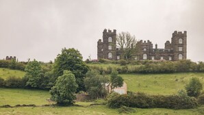 Un bâtiment historique en pierre, doté de deux tours, entouré d’un paysage verdoyant et d’arbres.