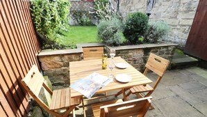 Une table en bois, dressée pour quatre personnes, avec un journal, des verres à vin et des assiettes.