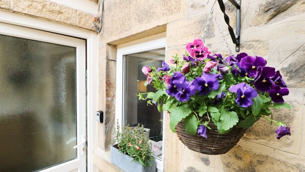 Un bâtiment en pierre orné d’un panier suspendu rempli de fleurs violettes et roses.