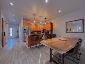 A modern kitchen with wooden cabinets, a stainless steel refrigerator, and a dining area with a wooden table and chairs.