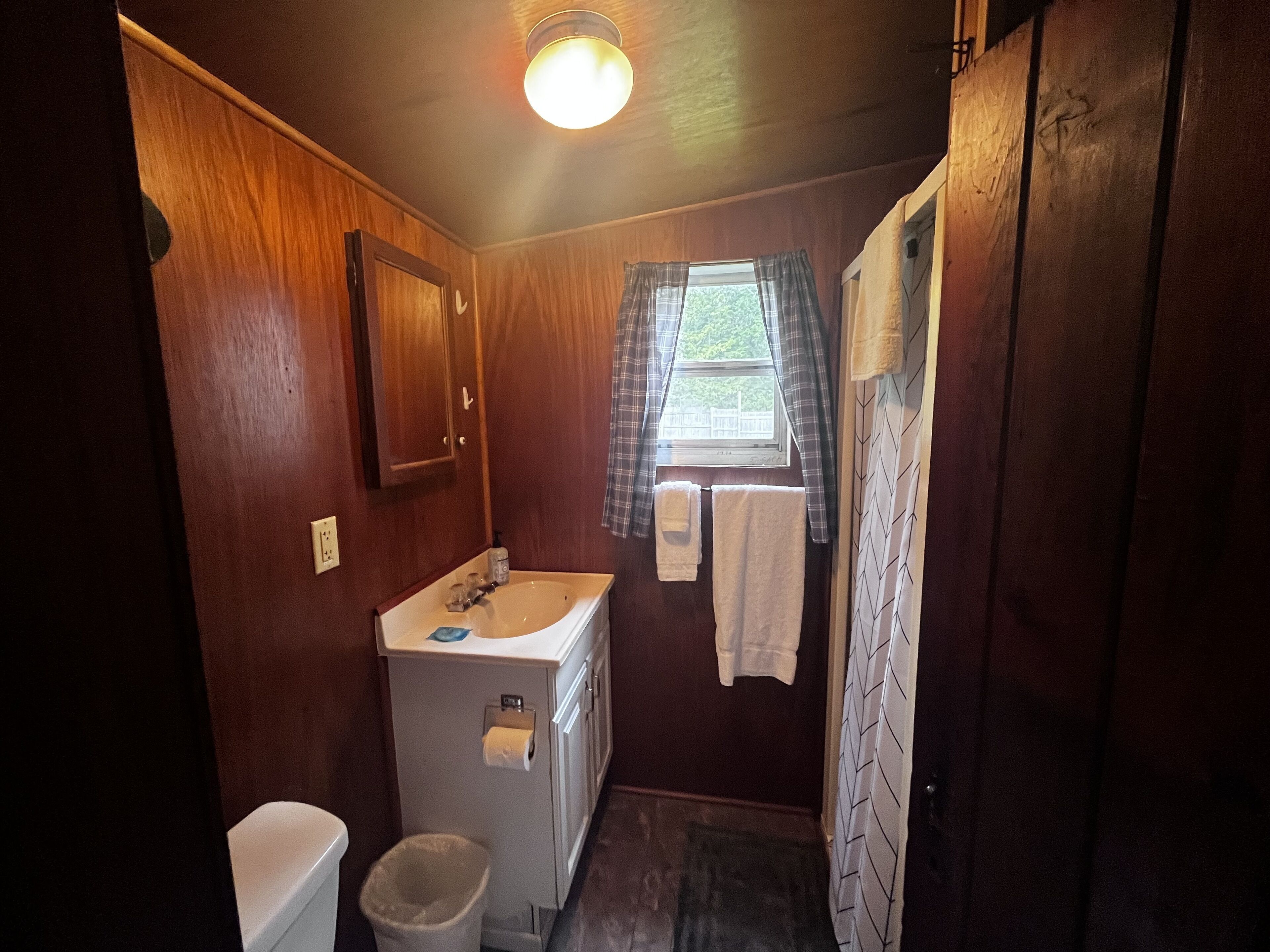 A compact bathroom with wooden walls, a white sink, a toilet, and a shower curtain.