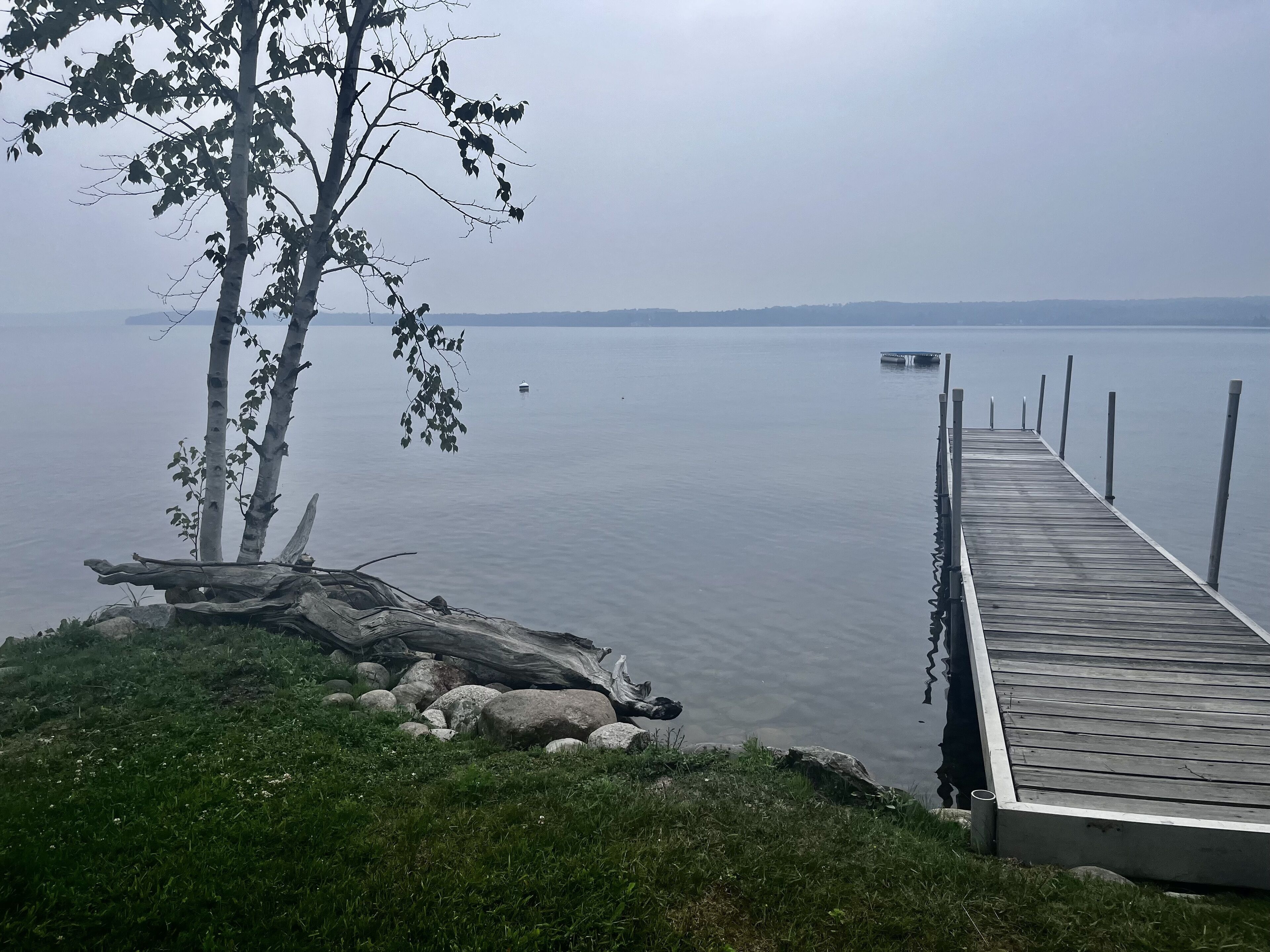 A wooden dock extending into calm water, surrounded by rocks and greenery.