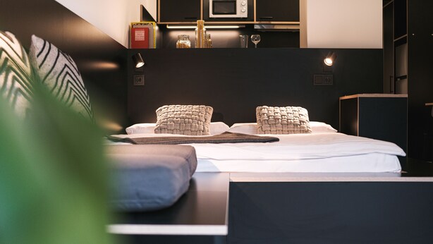 A modern bedroom with a neatly made bed, a bedside table, and a built-in bookshelf. - MoLiving - Design Hotel & Apartments Düsseldorf-Neuss (Neuss)