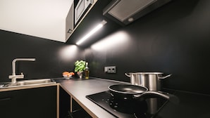 A modern kitchen with a black countertop, stainless steel appliances, and a pot on the stove. - MoLiving - Design Hotel & Apartments Düsseldorf-Neuss (Neuss)