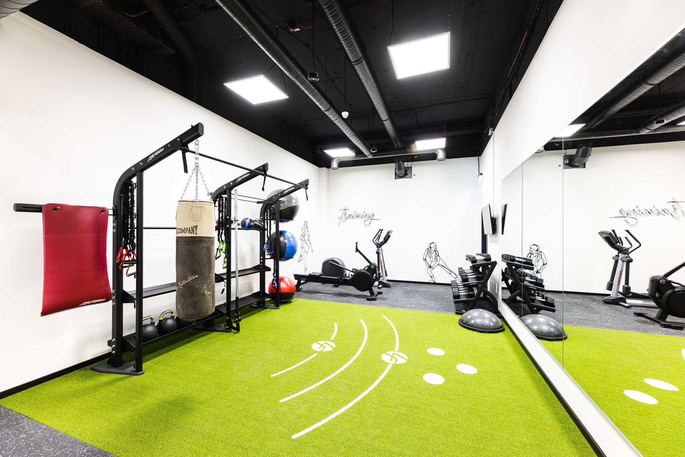 Et fitnessrum med træningsudstyr, grøn kunstgræs og en rød måtte.
