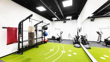 Et fitnessrum med træningsudstyr, grøn kunstgræs og en rød måtte.