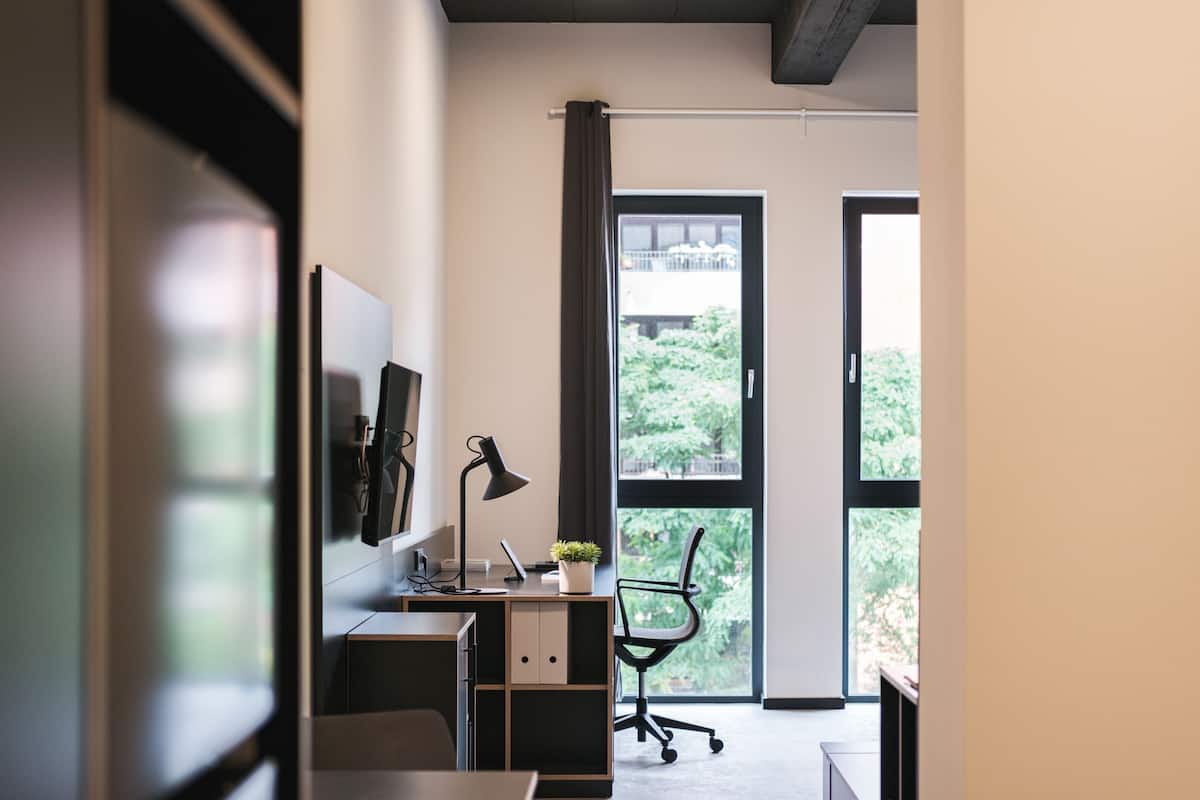 Un espace de bureau moderne comprenant un bureau, une chaise, une lampe et une vue sur la verdure environnante.