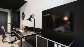 Un ufficio moderno con scrivania, sedia, computer, lampada e una grande TV a schermo piatto montata a parete.
