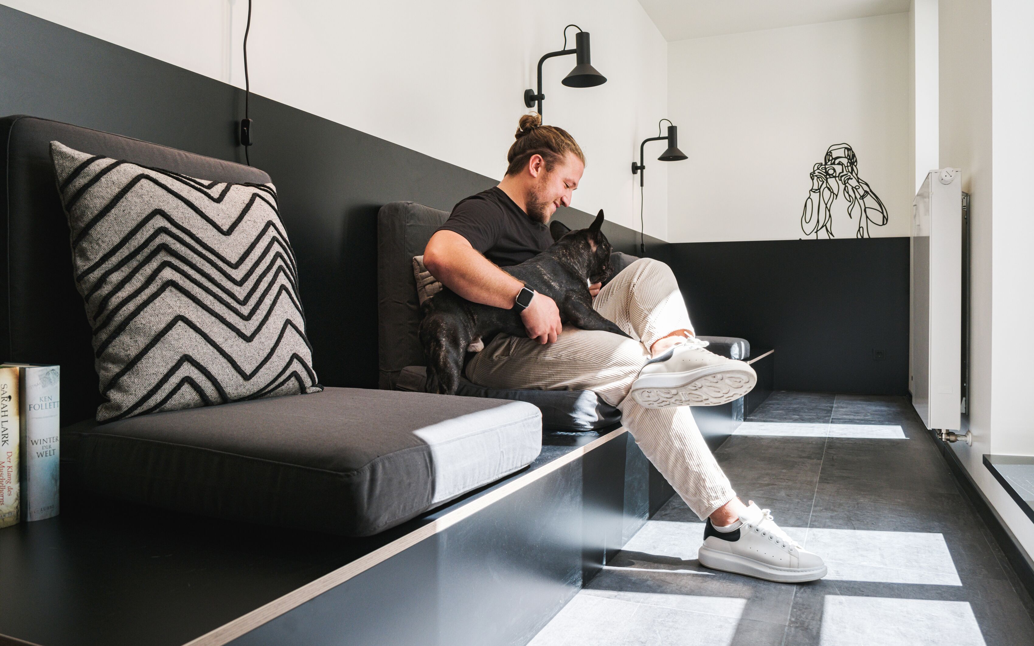 A person sitting on a black sofa with a chevron-patterned pillow, holding a cat.