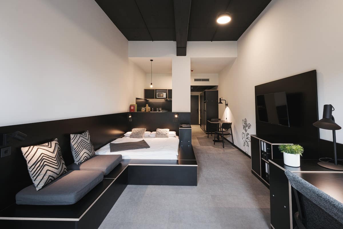 Une chambre d’hôtel moderne équipée d’un canapé, d’un petit bureau, d’une télévision et d’une kitchenette.