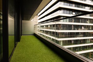 A modern building with multiple floors, large windows, and a green artificial grass area in the foreground. - The Wardian (London)