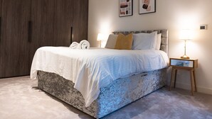 A bedroom with a bed, bedside lamps, a wardrobe, and two framed pictures on the wall. - The Wardian (London)