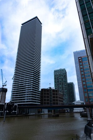 A tall, modern skyscraper with a unique, ribbed facade, surrounded by other high-rise buildings and a body of water. - The Wardian (London)