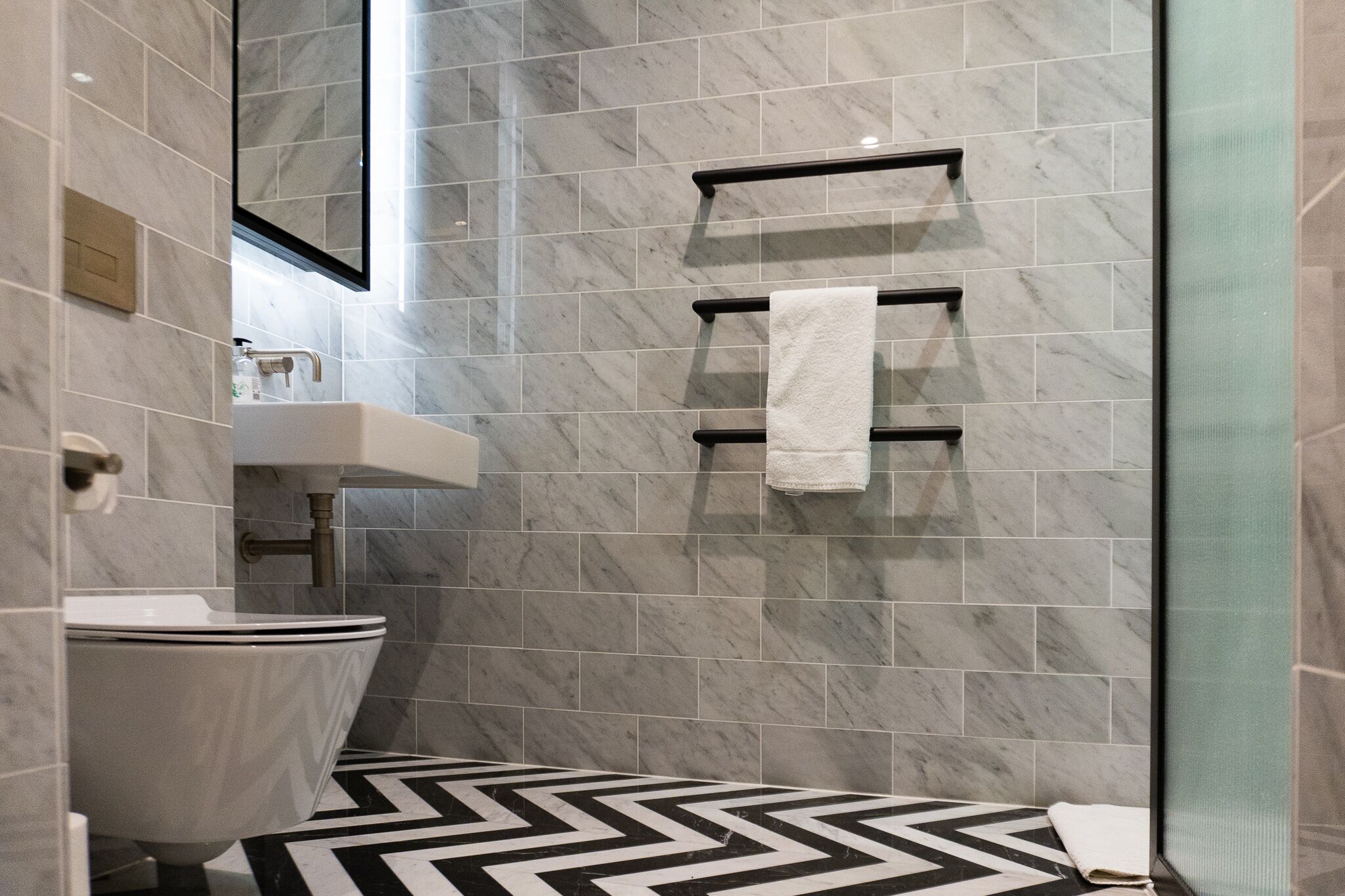 A modern bathroom with a toilet, sink, and towel rack against a marble wall.