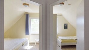 A mirrored view of a small, well-lit room with two beds, a window with curtains, and a radiator.