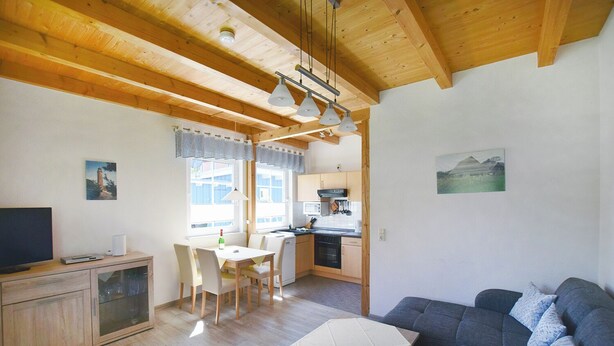 A cozy living room with a sofa and a dining area with a table and chairs. There is a kitchen area with a stove and cabinets.