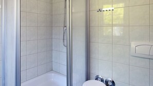 A bathroom with a glass-enclosed shower, white tiles, a small white stool, and a marble sink with starfish decoration.