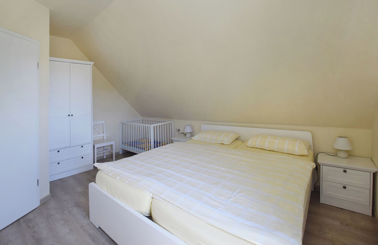 A bedroom with a bed, nightstands, a crib, and a wardrobe.