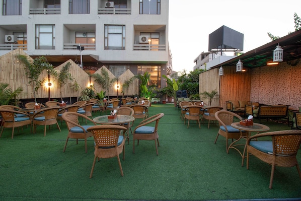 An outdoor seating area with wicker furniture and artificial grass, surrounded by buildings with balconies and windows.