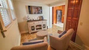 Un salon chaleureux avec un canapé, un pouf et un meuble blanc aux portes vitrées.