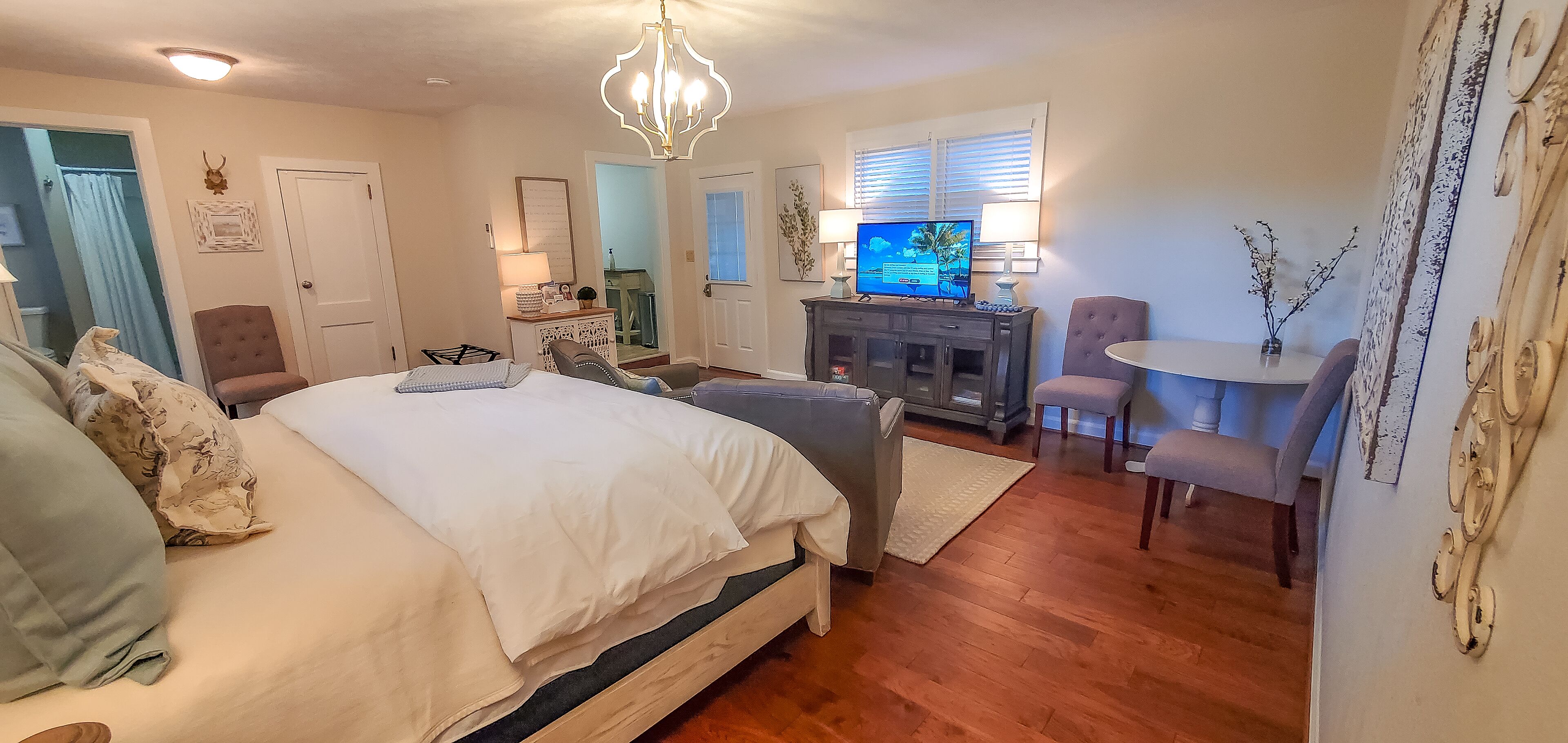 Une chambre avec un grand lit, une commode, une télévision et un fauteuil.