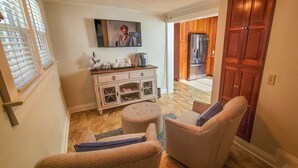 Una sala de estar acogedora con un sofá, un reposapiés y un mueble blanco con puertas de cristal.
