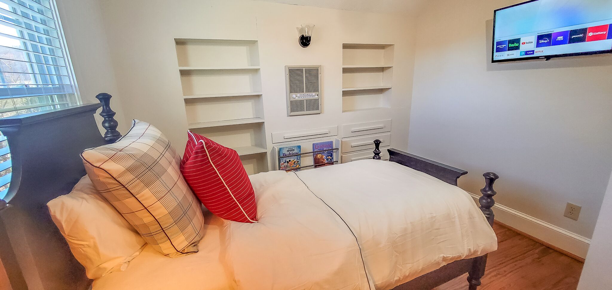 Une chambre à coucher avec un lit, un téléviseur fixé au mur et des étagères intégrées.