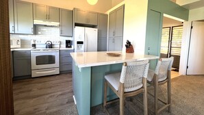 Eine moderne Küche mit grauen Schränken, einem weißen Kühlschrank und einer zentralen Kochinsel mit zwei Korbstühlen.