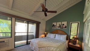 Ein Schlafzimmer mit einem großen Bett, einem Deckenventilator, einem Fenster mit Jalousien und Kunstwerken an der Wand.