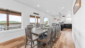 Un comedor amplio con una mesa y sillas de madera, ventanas grandes con vistas al exterior y una cocina equipada con electrodomésticos modernos.