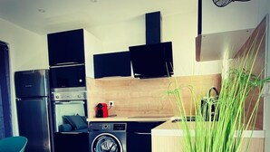 A modern kitchen with stainless steel appliances, a built-in oven, a washing machine, and a wooden backsplash. - Appartement Zen 4 pers. à Canet - Balconies, sea & mountain views, private parking (Canet-en-Roussillon)