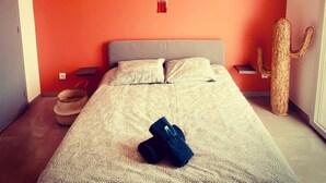 Une chambre avec un lit, un luminaire suspendu, un climatiseur fixé au mur, une décoration en forme de cactus et une décoration murale en macramé.