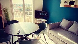 Un salon moderne avec une table ronde, deux chaises, un canapé, un téléviseur et un balcon avec vue.