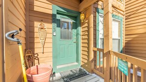 Une maison en bois avec une porte verte, un panneau d’avertissement, un portail en métal et un porche recouvert de neige.