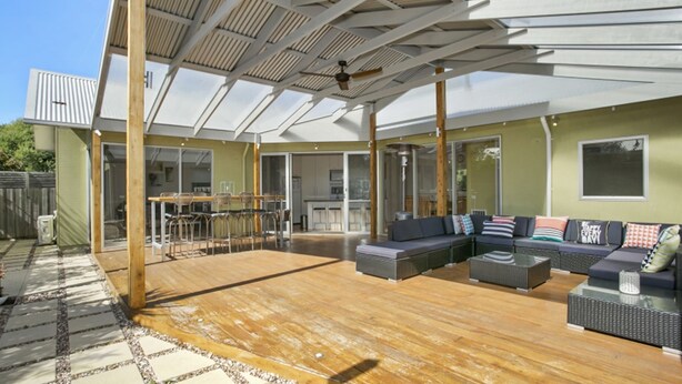 Ein Außenbereich mit Terrassendeck, einem Esstisch mit Stühlen, einer Sofagarnitur und einem Deckenventilator.