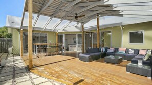 Un espace extérieur aménagé en terrasse, avec une plateforme en bois, une table à manger et des chaises, un ensemble de canapés et un ventilateur de plafond.
